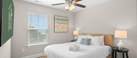 A bedroom with a bed, two bedside tables, a ceiling fan, a window with blinds, and a painting on the wall.