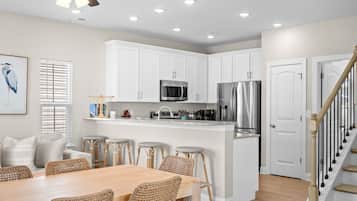 Una cocina moderna con armarios blancos, electrodomésticos de acero inoxidable y un comedor con sillas de mimbre.