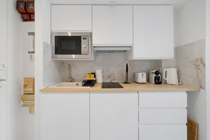 Una cocina moderna con armarios blancos, microondas integrado, cafetera y tostadora.