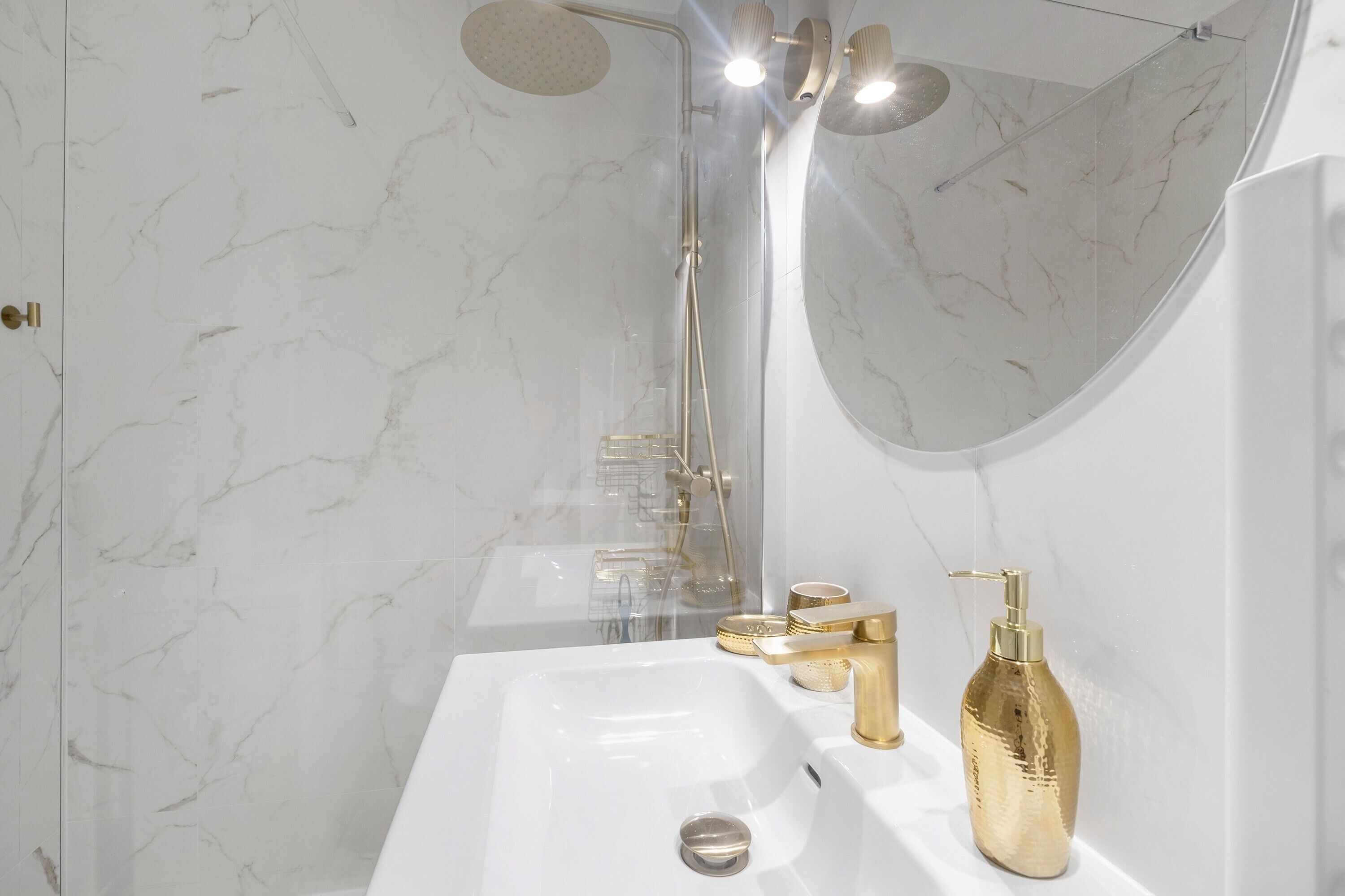 Baño con lavamanos blanco, accesorios dorados, ducha de mano y un espejo grande.