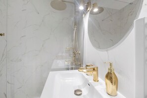 A bathroom with a white sink, gold fixtures, a handheld showerhead, and a large mirror. - Studio Apartment 'Cosy and Central' with Wi-Fi and Air Conditioning (Nice)
