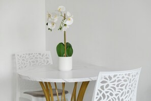 A round white table with a potted orchid, two white chairs with a leaf pattern, and a plain white wall. - Studio Apartment 'Cosy and Central' with Wi-Fi and Air Conditioning (Nice)