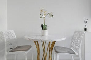 A round table with a white marble top, two chairs with gold legs, and a white orchid in a white pot. - Studio Apartment 'Cosy and Central' with Wi-Fi and Air Conditioning (Nice)