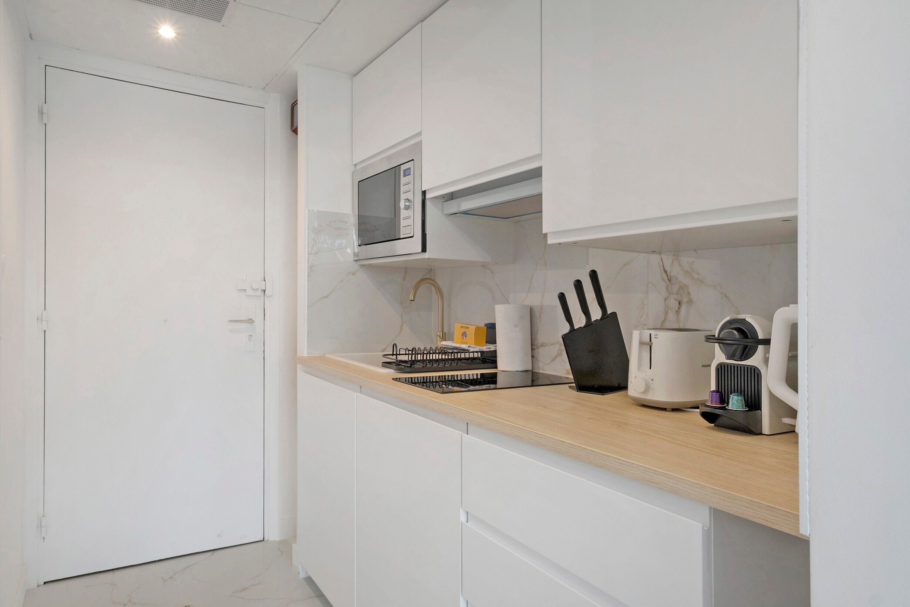 Una cocina moderna con armarios blancos, microondas, cafetera y tostadora.