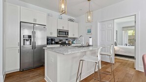 Una cocina moderna con armarios blancos, electrodomésticos de acero inoxidable y una isla central con taburetes de bar.