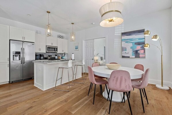 Una cocina moderna con armarios blancos, electrodomésticos de acero inoxidable y una isla central con taburetes de bar.