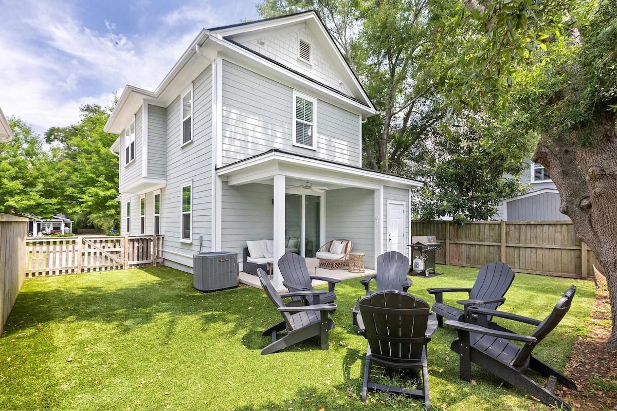 Une maison à deux étages avec un porche couvert, une pelouse et des fauteuils Adirondack.