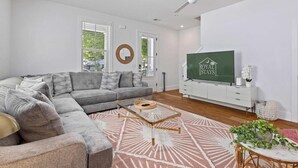 Una sala de estar moderna con un sofá modular, una mesa de centro de vidrio y un televisor de pantalla plana sobre un mueble blanco.