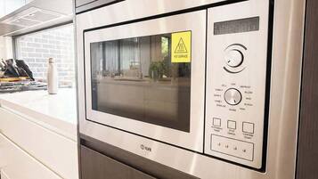 A stainless steel microwave oven with a digital display and control panel, set in a modern kitchen with wooden cabinets and a window.