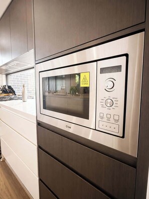 A stainless steel microwave oven with a digital display and control panel, set in a modern kitchen with wooden cabinets and a window. - Modern Ryde Retreat: WiFi, Walk to Cafés/Shops (Ryde)