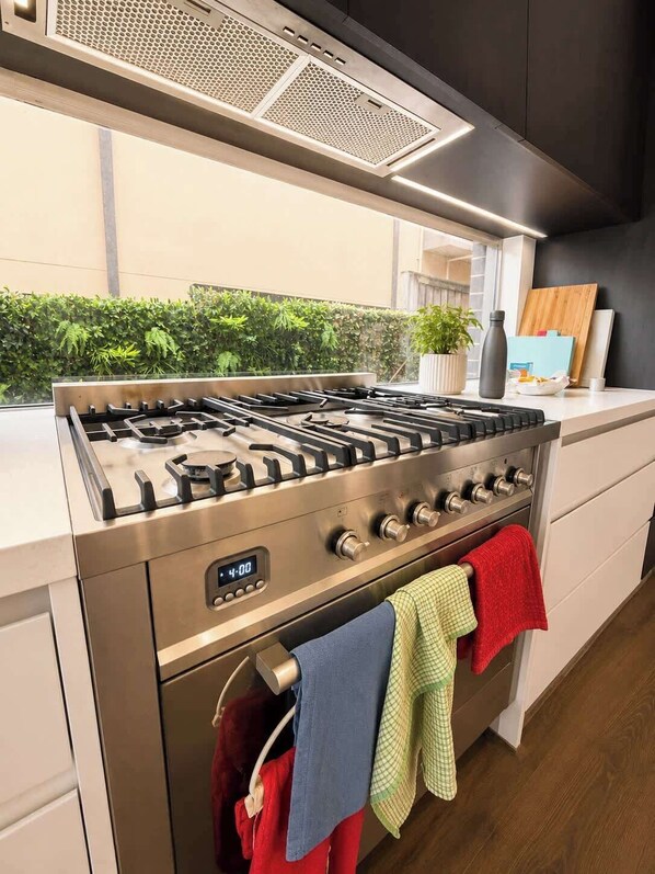 A modern kitchen with a stainless steel stove, a digital clock, and a view of greenery outside.