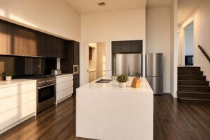 A modern kitchen with a central island, stainless steel appliances, and a dark wood floor.