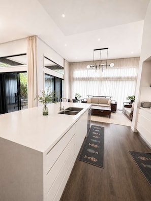 A modern kitchen with a large island, a dining area with a sofa, and a view of greenery outside.