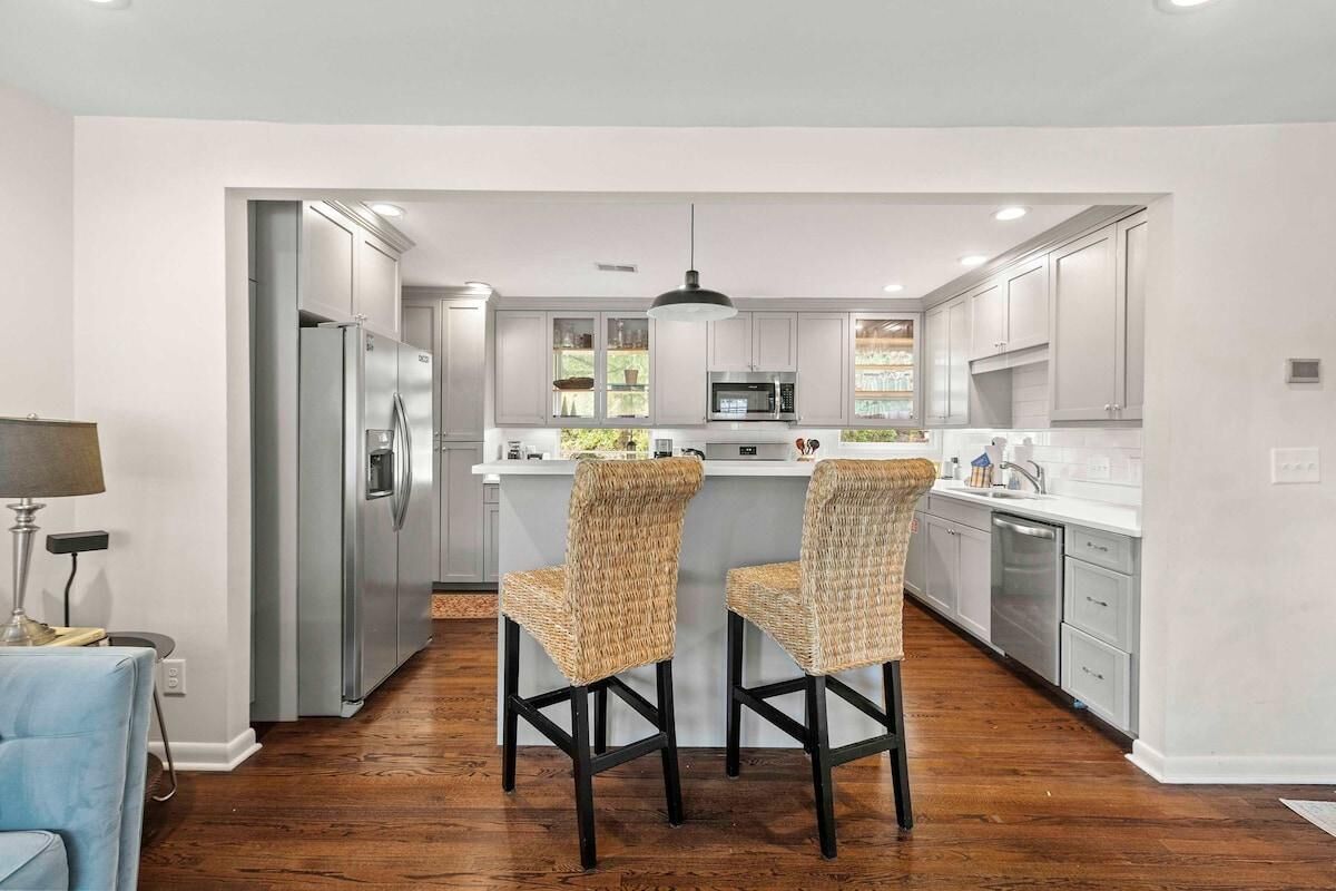 A modern kitchen with stainless steel appliances, a central island with bar stools, and a view into the adjacent living area.