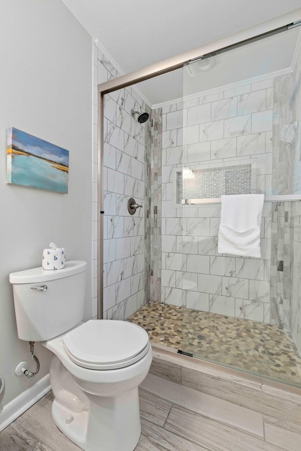 A modern bathroom with a toilet, a glass-enclosed shower, and a marble-tiled wall.