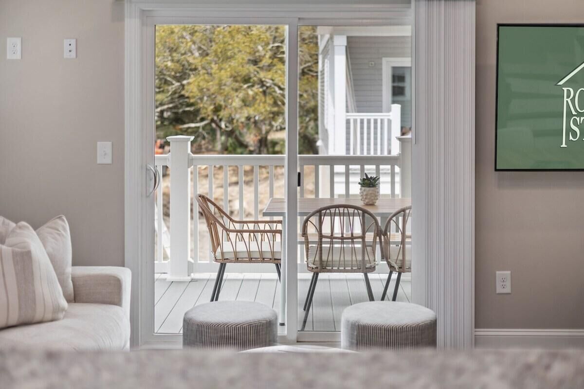 A living room with a sliding glass door leading to a balcony with wicker chairs and ottomans.