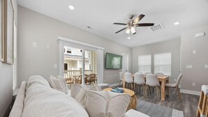 Ein modernes Wohnzimmer mit Sofa, Esstisch und Stühlen. Es gibt einen Deckenventilator und einen Blick auf den Balkon.