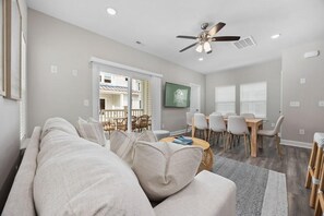A modern living room with a sofa, dining table, and chairs. There is a ceiling fan and a view of the outside balcony. - Ace Basin-across Ocean-pet Friendly (Myrtle Beach)