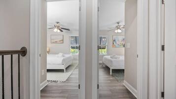 A hallway leading to a bedroom with a bed, a ceiling fan, and artwork on the walls.