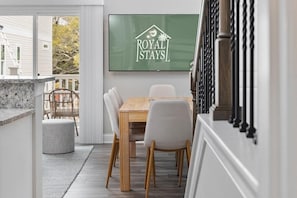 A dining area with a wooden table and chairs, a television displaying 'ROYAL STAYS', and a view of a white building outside. - Ace Basin-across Ocean-pet Friendly (Myrtle Beach)