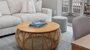 Ein Wohnzimmer mit einem runden Korbtisch, einem grauen Sofa und einem gestreiften Hocker.