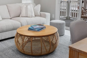 A living room with a round wicker coffee table, a grey sofa, and a striped ottoman. - Ace Basin-across Ocean-pet Friendly (Myrtle Beach)