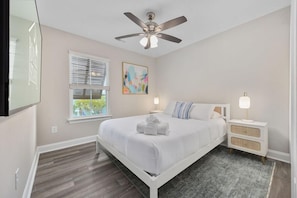A bedroom with a bed, a ceiling fan, a window with blinds, a bedside table with a lamp, and a painting on the wall. - Ace Basin-across Ocean-pet Friendly (Myrtle Beach)