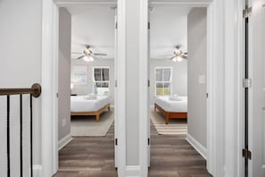 Ein Flur, der zu einem Schlafzimmer führt, mit einem Bett, einem Deckenventilator und einem Fenster mit Jalousien.
