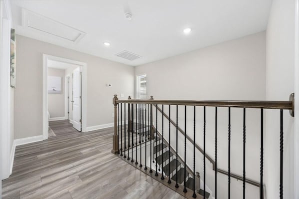 Una escalera con barandilla de madera y balaustres negros, que conduce a un rellano con una puerta.