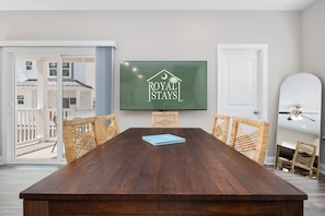 A conference room with a wooden table, wicker chairs, a TV screen displaying 'ROYAL STAYS', and a view of the outside deck. - Sea Cloud-across Ocean-pet Friendly! (Myrtle Beach)