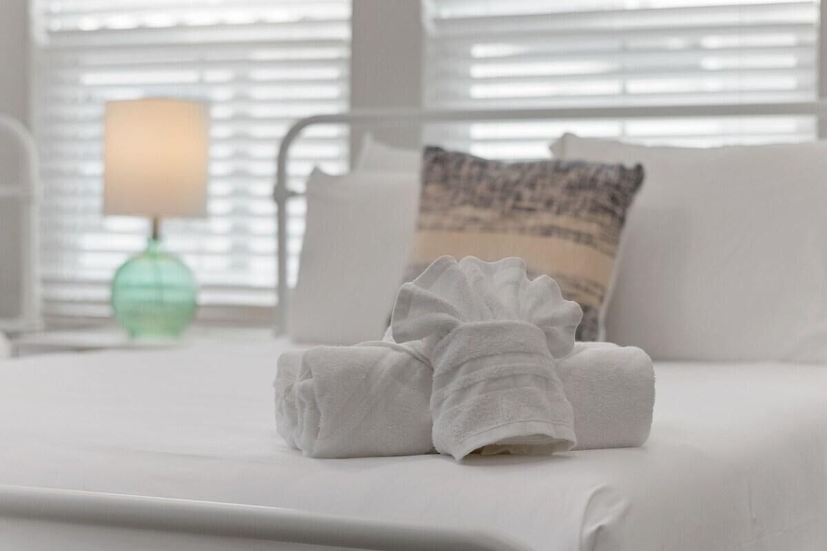 A neatly made bed with white bedding and a folded white towel on top.