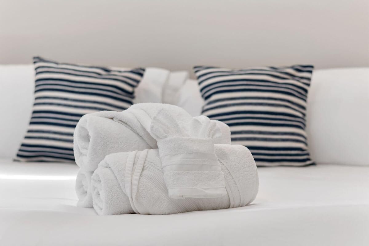 Ein ordentlich bezogenes Bett mit weißer Bettwäsche und zwei gestreiften Kissen.