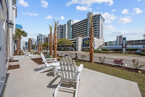 A hotel with a modern design, featuring a paved outdoor area with white Adirondack chairs and palm trees. - Sea Cloud-across Ocean-pet Friendly! (Myrtle Beach)