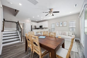 A modern kitchen with white cabinets, a dining area with a wooden table and wicker chairs, a staircase, and a ceiling fan. - Sea Cloud-across Ocean-pet Friendly! (Myrtle Beach)
