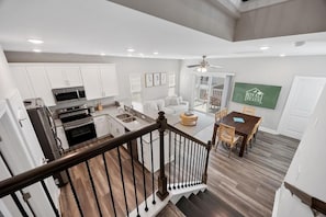 Amplia sala de estar con escalera, una mesa de comedor y cocina con armarios blancos y electrodomésticos modernos.