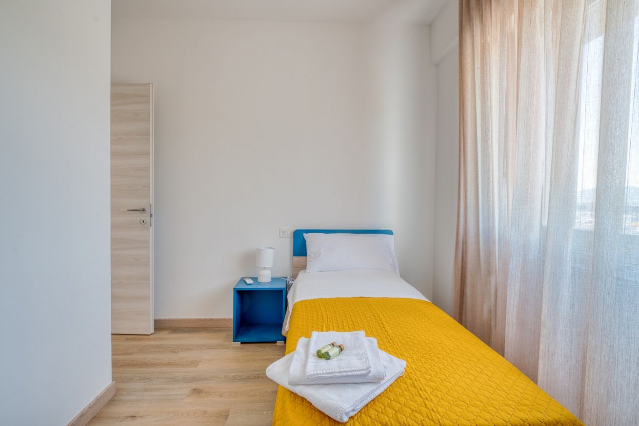 Una habitación de hotel con cama, mesita de noche, una puerta y una ventana con cortinas.