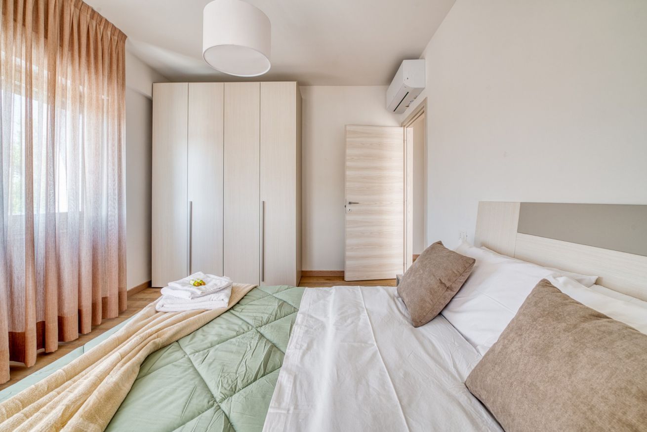 A bedroom with a bed, a wardrobe, a hanging light fixture, and an air conditioning unit.