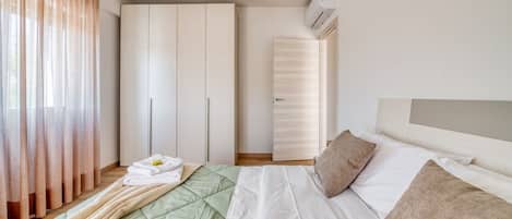 A bedroom with a bed, a wardrobe, a hanging light fixture, and an air conditioning unit.