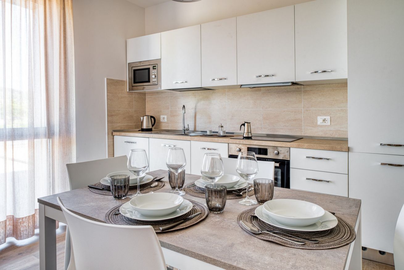 A modern kitchen with white cabinets, a microwave, and a dining table set for six with plates, glasses, and cutlery.