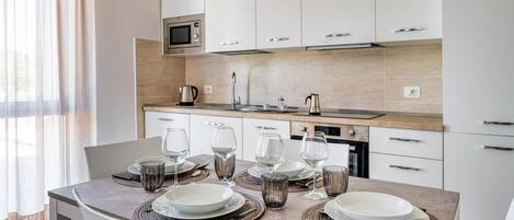 A modern kitchen with white cabinets, a microwave, and a dining table set for six with plates, glasses, and cutlery.