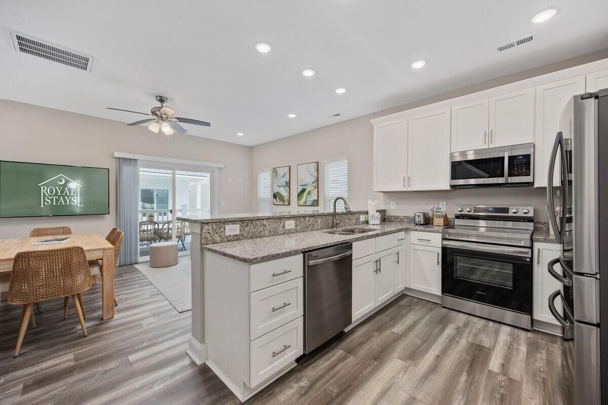 A modern kitchen with white cabinets, stainless steel appliances, and a dining area with wicker chairs.