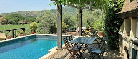A wooden deck with a pool, outdoor furniture, and a pergola with vines.
