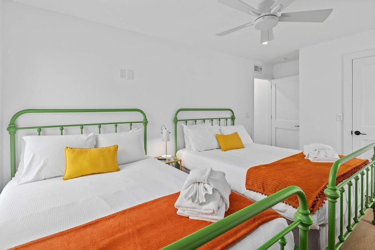 Habitació d'hotel amb dos llits, cadascun amb roba de llit blanca i ambres a les capçaleres. Hi ha llençols de color taronja sobre els llits, i una tovallola blanca plegada al llit.