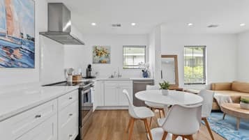 A modern kitchen with white cabinetry, a central island, and a dining area with white chairs.
