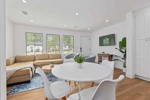 A modern living room with a beige sofa, white chairs, a round table, and a TV on the wall. - Suite Magnolia-hot Tub-pet Friendly, Mins 2 DT (Charleston)
