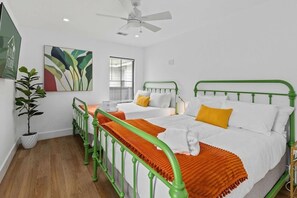 Quarto com duas camas, um ventilador de teto, uma janela com persianas e um vaso de planta.