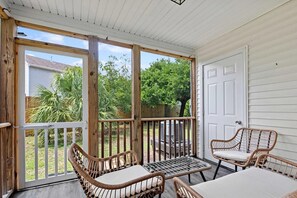 Eine überdachte Veranda mit Korbmöbeln, einer Tür und Blick auf den Garten.