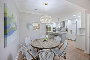 Une cuisine moderne avec des meubles blancs, une table à manger ronde en bois entourée de chaises en osier et un luminaire suspendu.