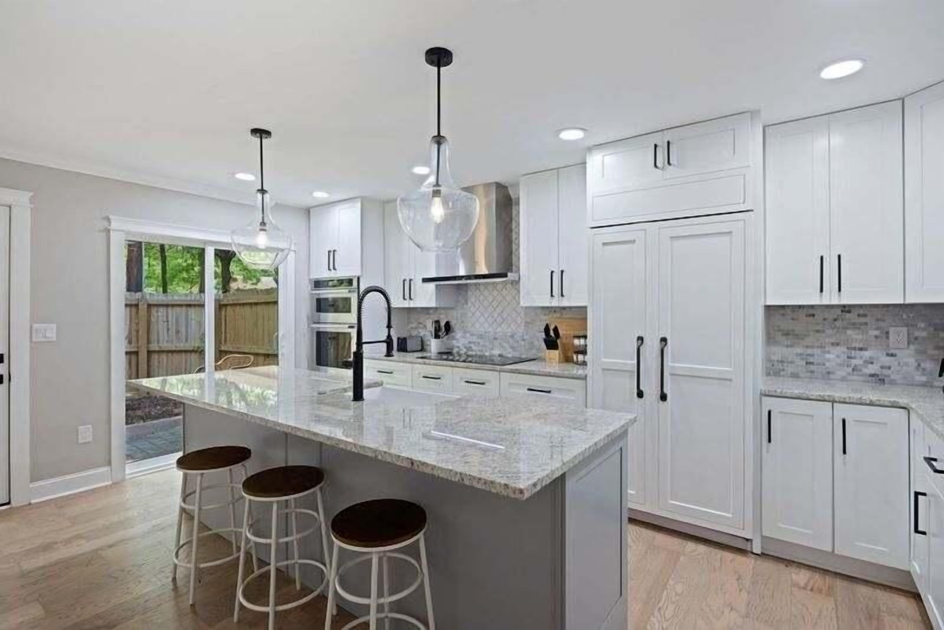 A modern kitchen with white cabinetry, a central island with stools, pendant lighting, and a view of the outdoors.