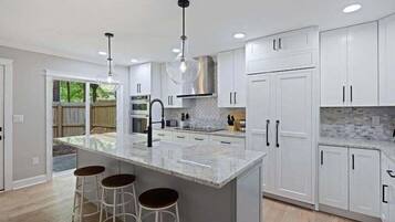A modern kitchen with white cabinetry, a central island with stools, pendant lighting, and a view of the outdoors.